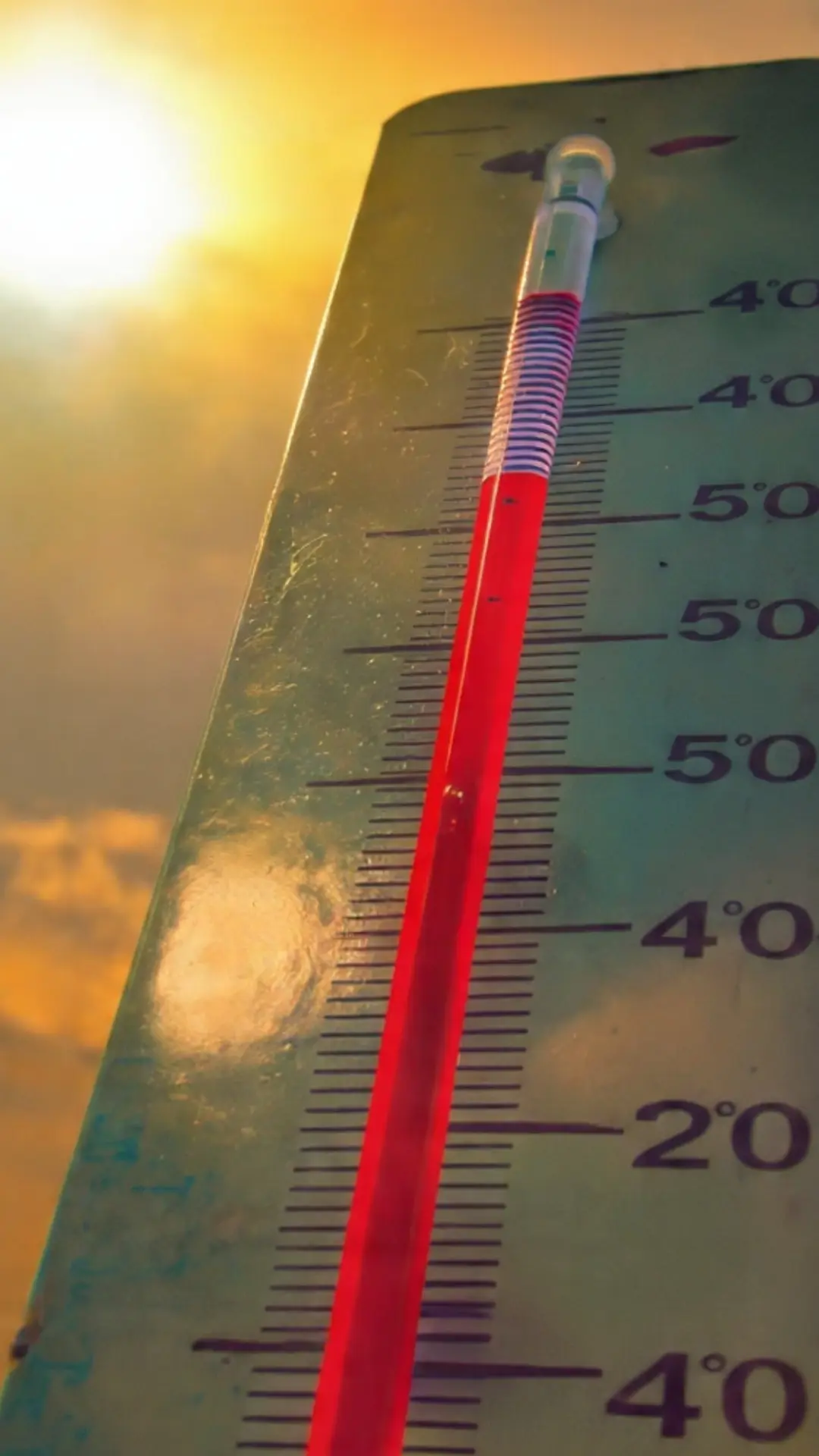 Portrait image of thermometer showing high temperature under bright sun and orange sky representing global warming and heatwave