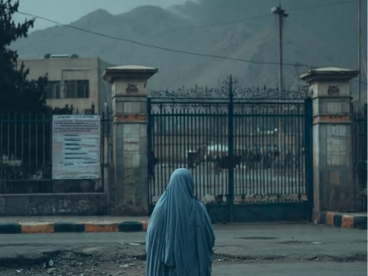 Photorealistic image of an Afghan woman barred from a closed school, representing the loss of women’s education and rights in Afghanistan since 2021. The image is done in a respectful, documentary style to match the tone of your piece about rights reversal, economic impact.